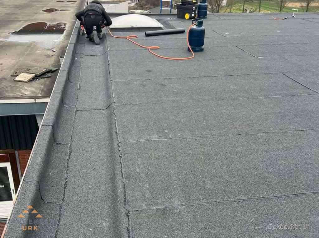 Dakdekker repareert bitumen dakbedekking op groot plat dak in Urk